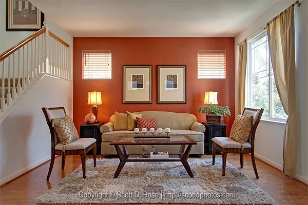 Staged living room interior with terracotta accent wall, sofa, framed artwork, and staircase photographed by Scott DuBose