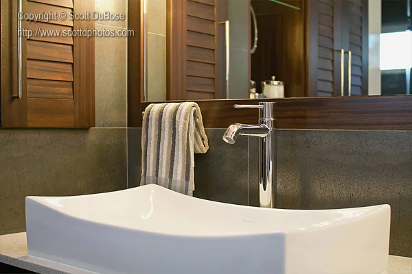 Close-up of a modern vessel sink with chrome faucet, dark stone wall surround, and wood shutter panel photographed by Scott DuBose