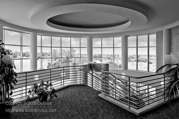 Black-and-white photo of a commercial building interior with circular rotunda ceiling, curved mezzanine railing, and panoramic windows photographed by Scott DuBose