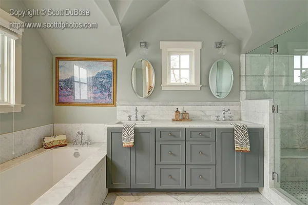 Elegant master bathroom with marble soaking tub, double gray vanity, oval mirrors, and glass shower enclosure photographed by Scott DuBose