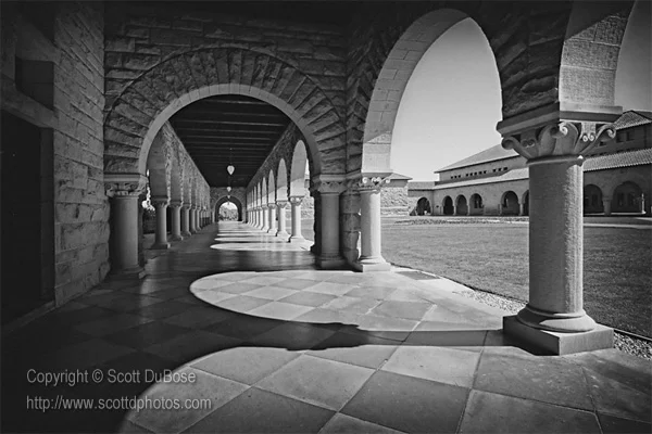 Black-and-white photograph of a sandstone arcade colonnade with arched walkway and open courtyard photographed by Scott DuBose